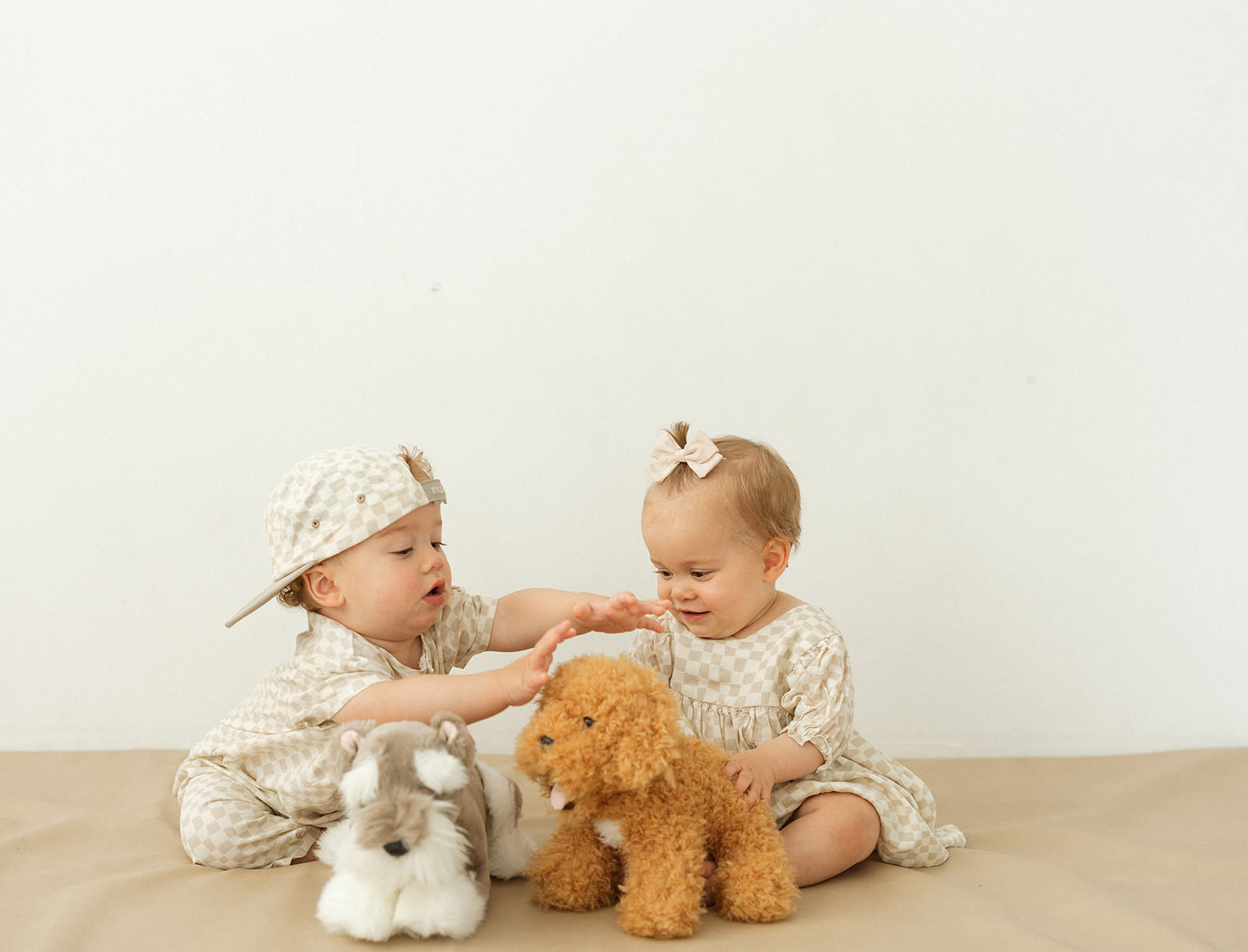 Twin babies play with stuffed animals in a photography studio.