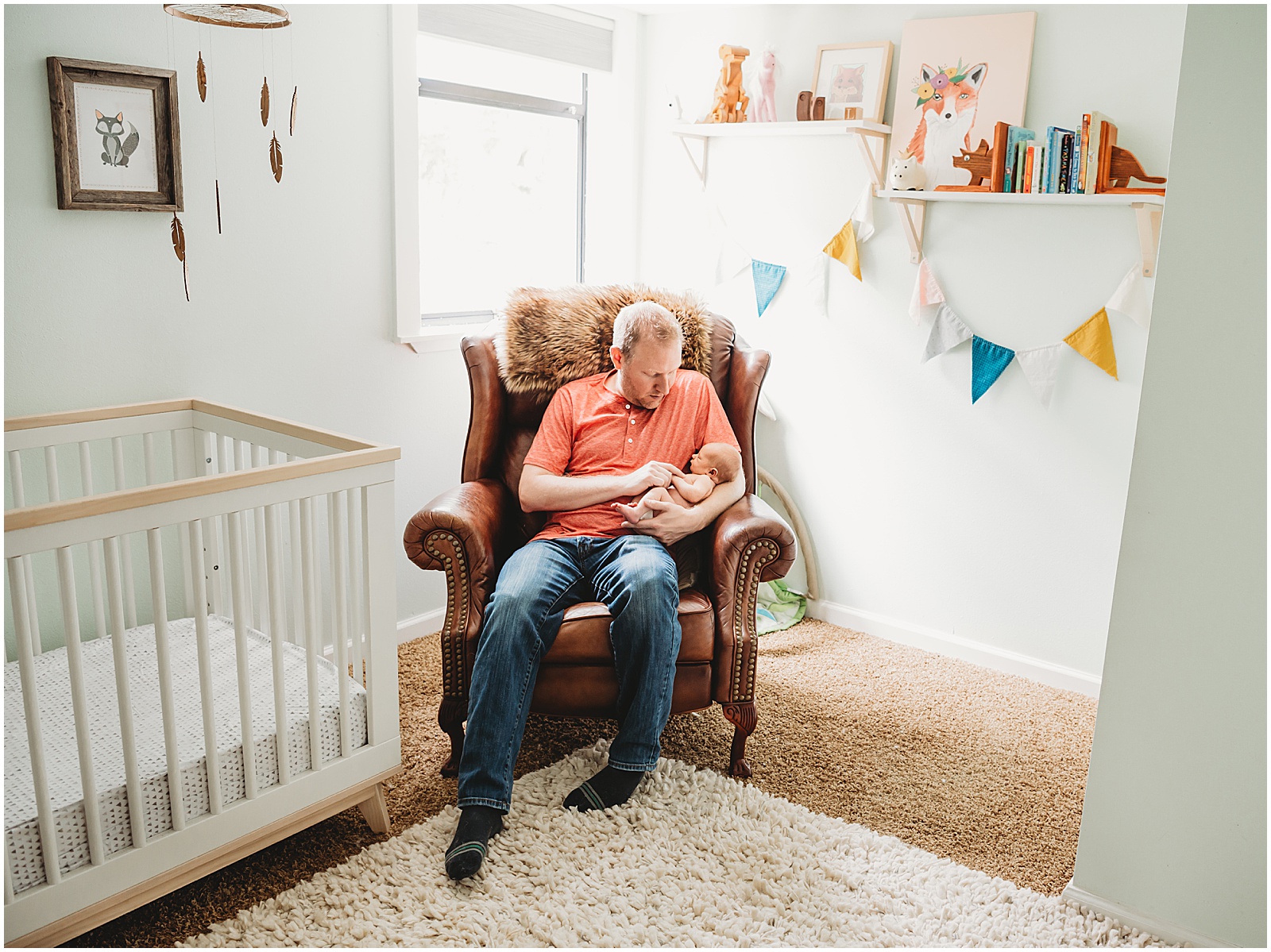 A father holds a newborn in an armchair listed on a newborn checklist.