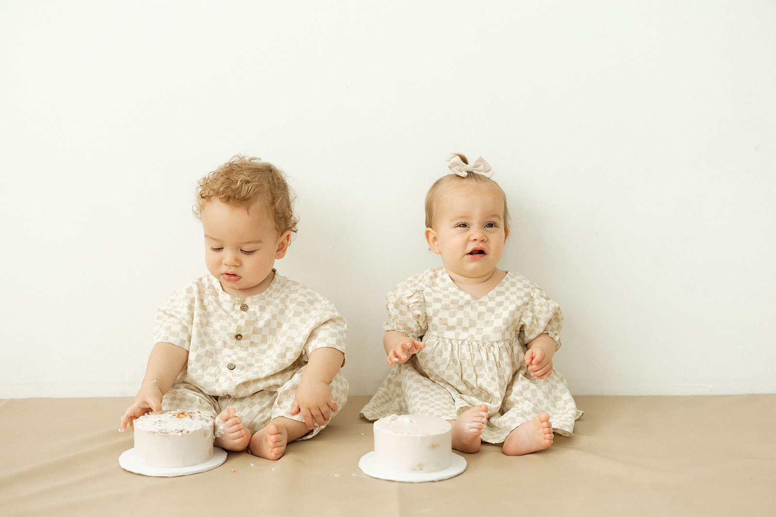 Twin babies eat cakes in a first birthday photoshoot in a studio.