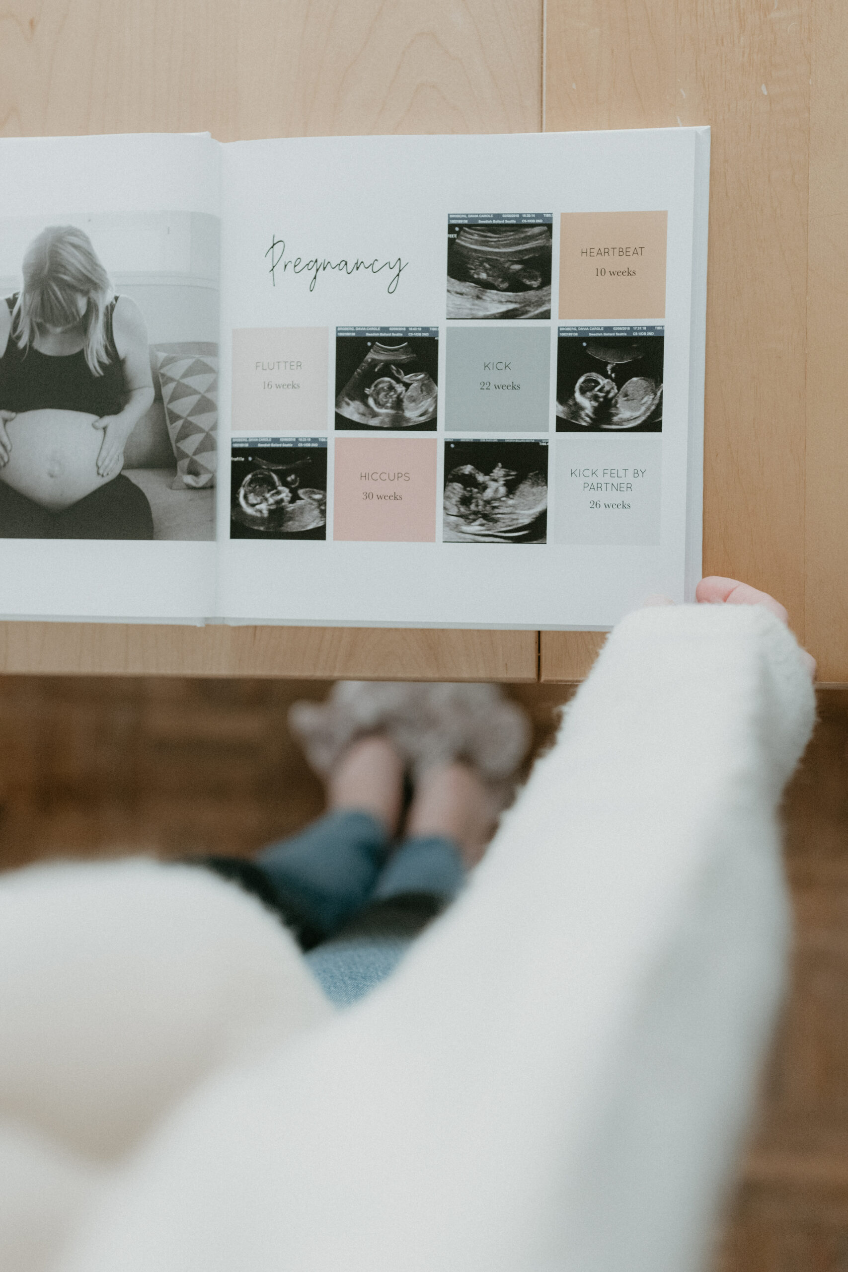 A woman stands beside a table with a book open to a list of baby milestones.