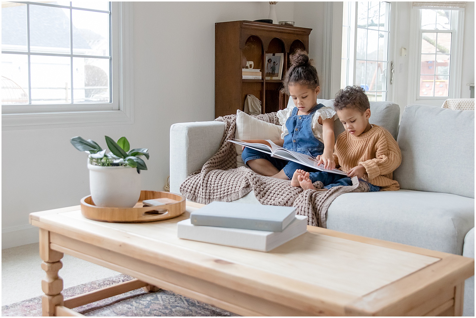 Two children look through their custom baby books on a couch in a sunlit living room.