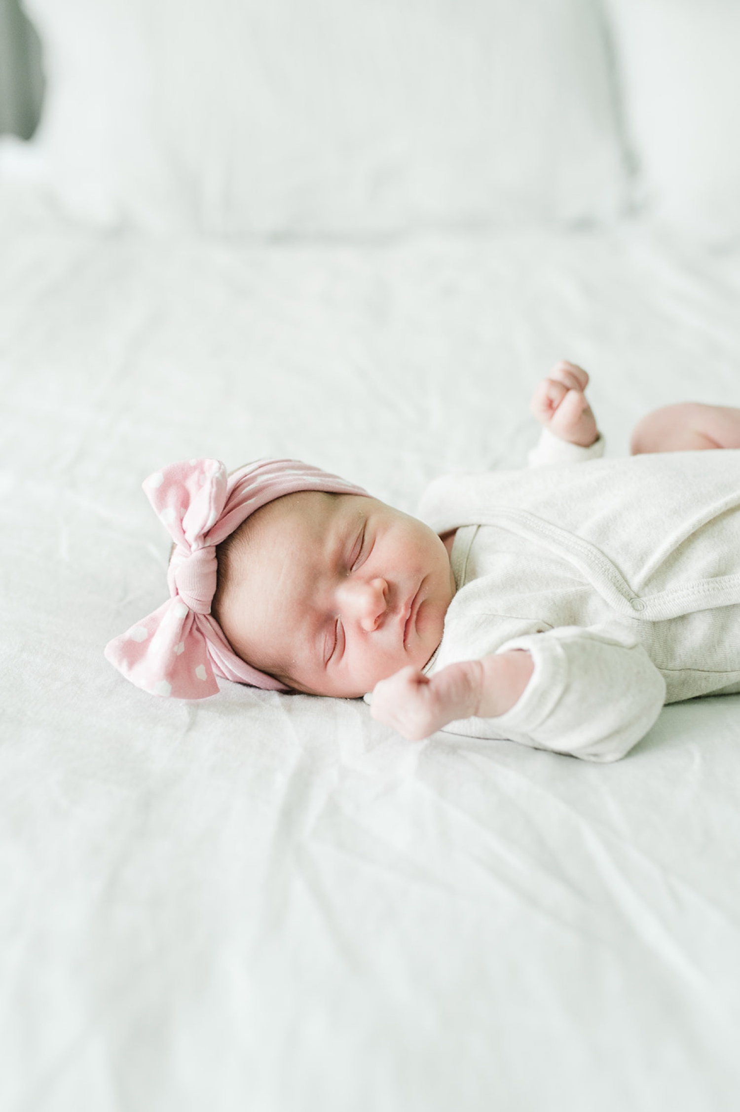 A newborn lays on a white bed during a lifestyle photoshoot.