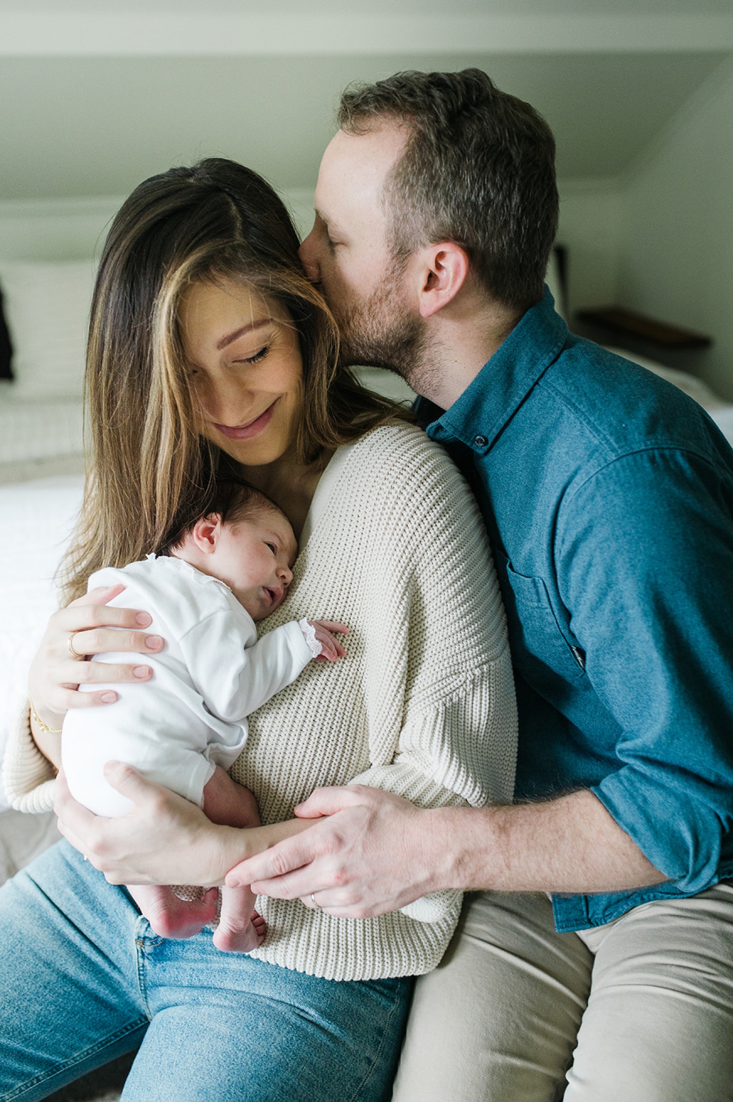 A man kisses his wife's cheek as she snuggles their newborn.