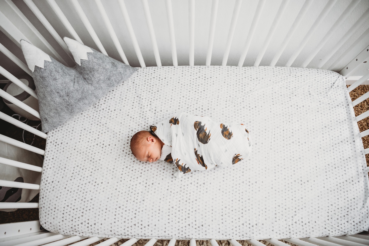 A swaddled baby lies in a crib.