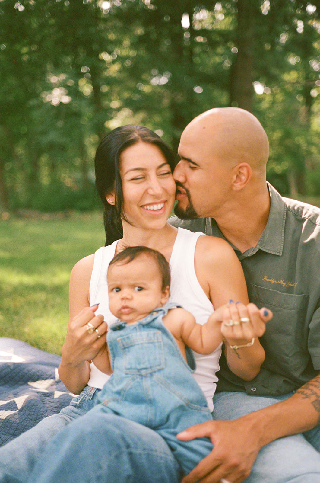 A family sits on a blanket in a backyard for a milestone photoshoot at home.