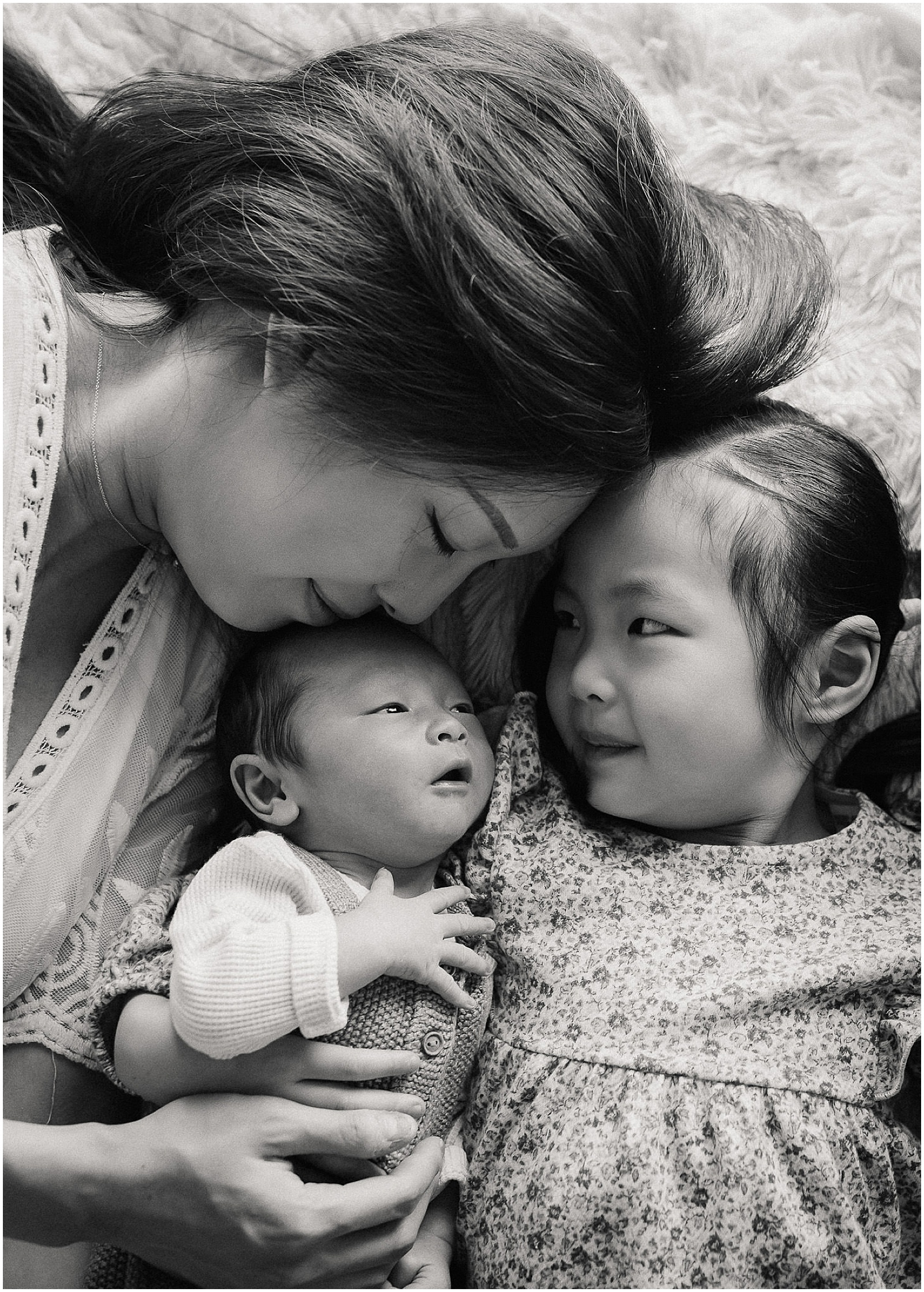 A mother and toddler cuddle a newborn baby.