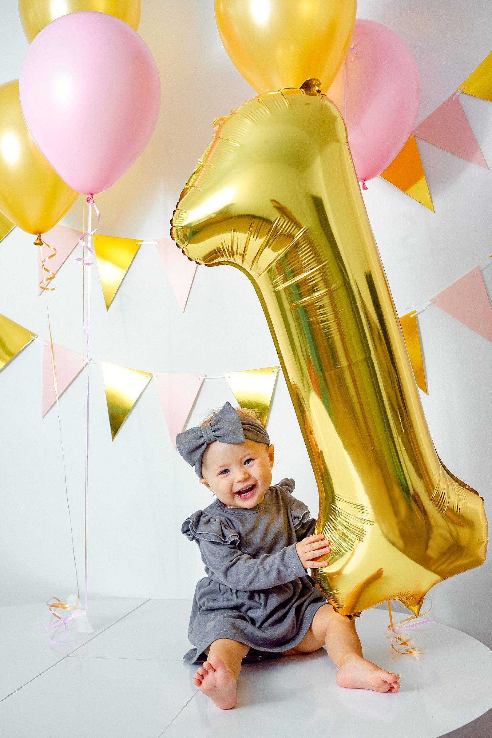 A baby sits holding a helium balloon to model 1st birthday photoshoot ideas.