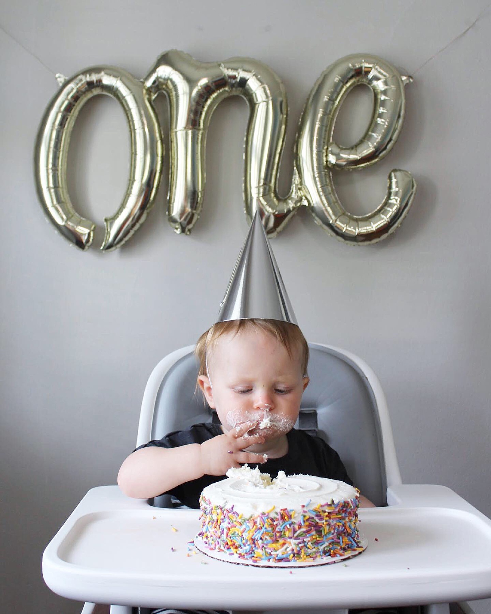 A baby sits under a balloon eating cake to model 1st birthday photoshoot ideas.