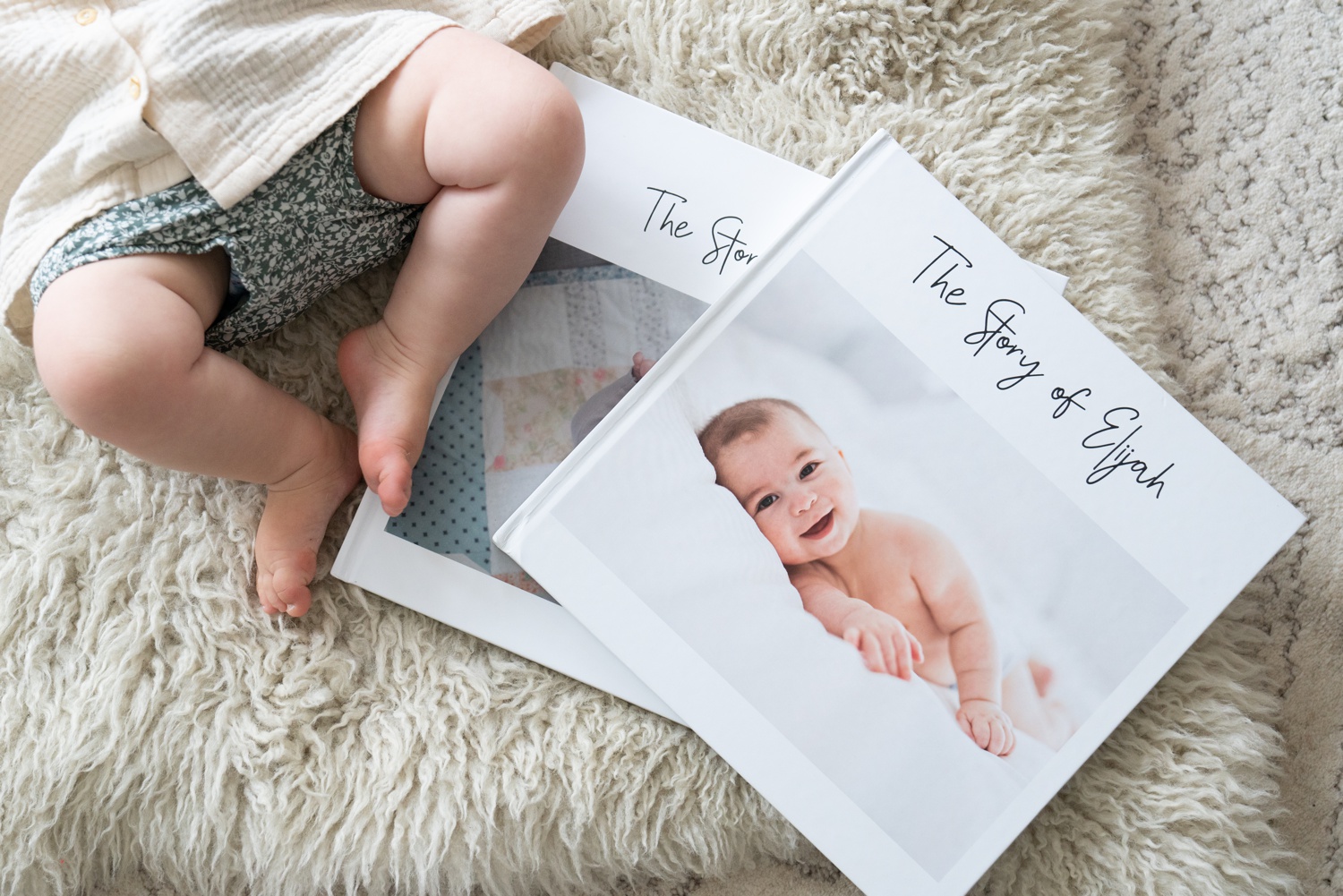 A baby lays on a rug next to photo albums with different memory book title ideas.