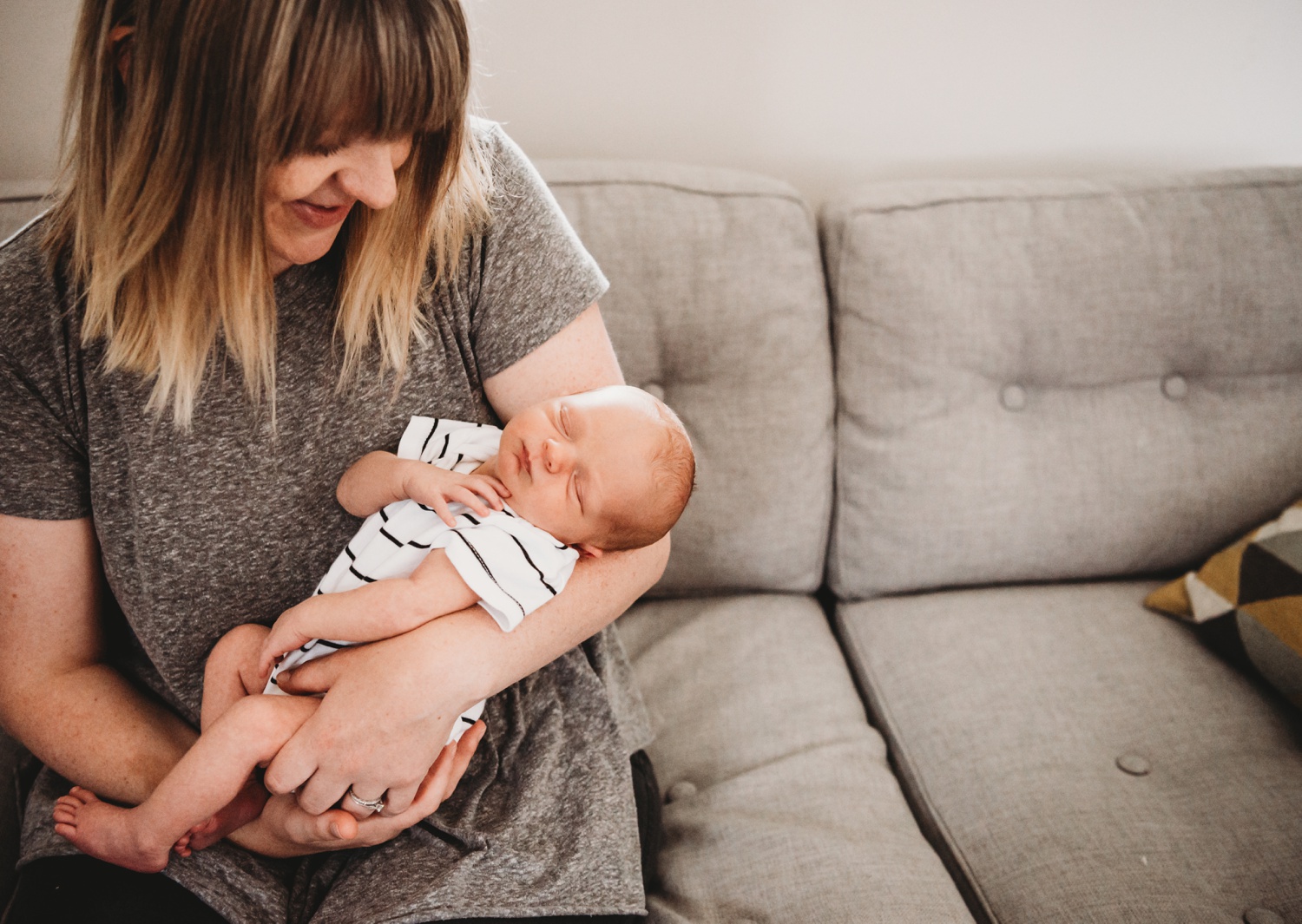 A mother holds a newborn on a couch after learning how to take newborn photos.