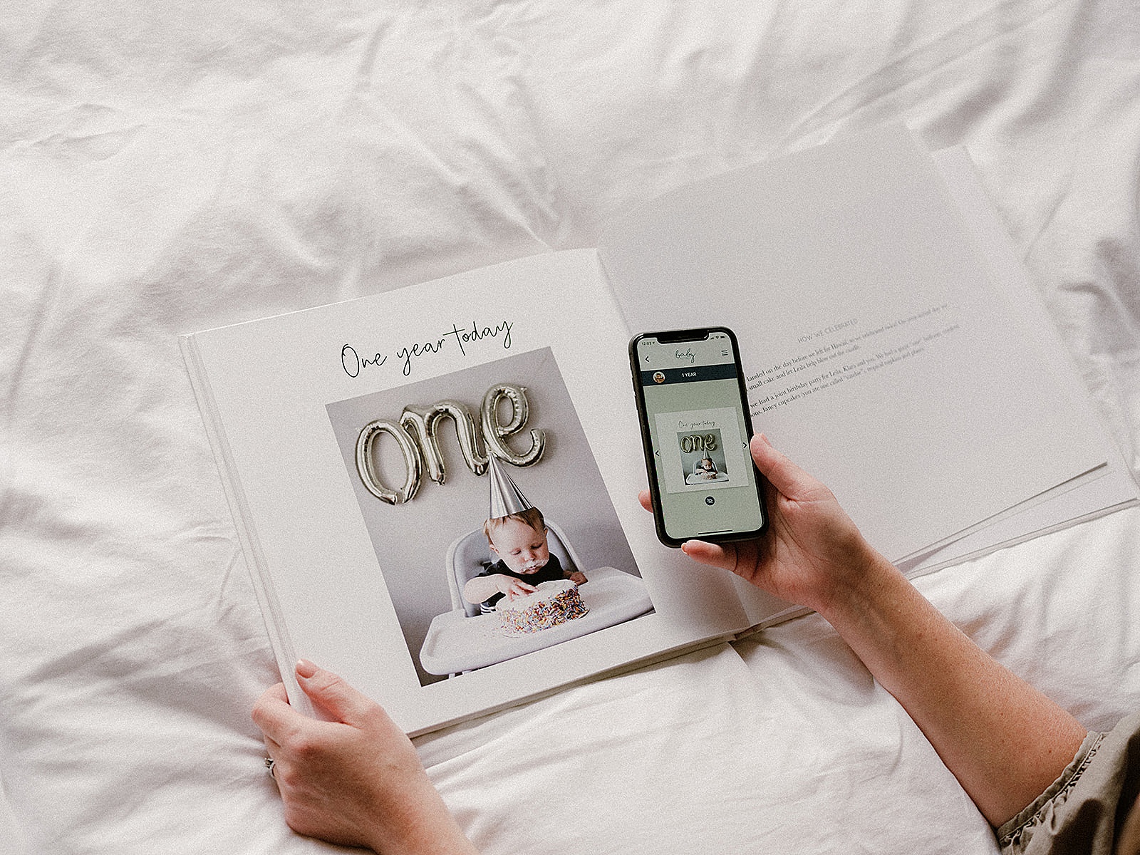 A woman holds her phone open to a digital baby book above a printed book.