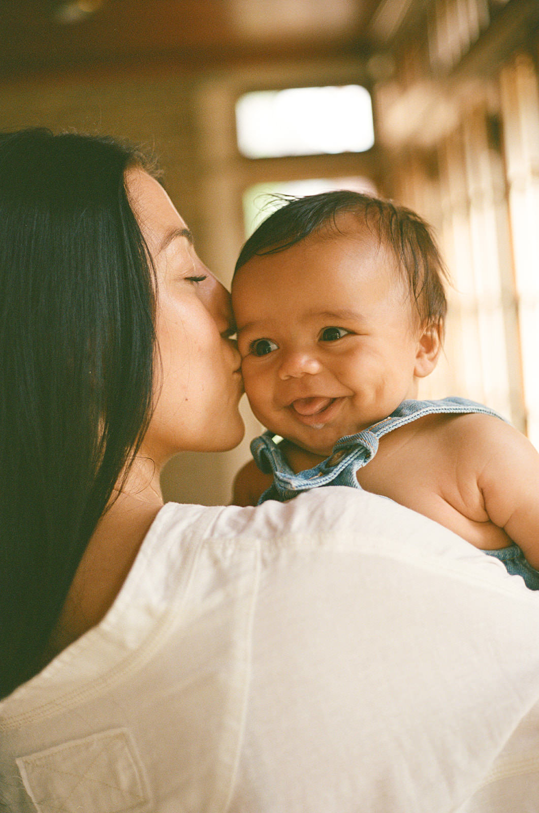 A mother kisses a baby's cheek for lifestyle milestone photoshoot ideas.