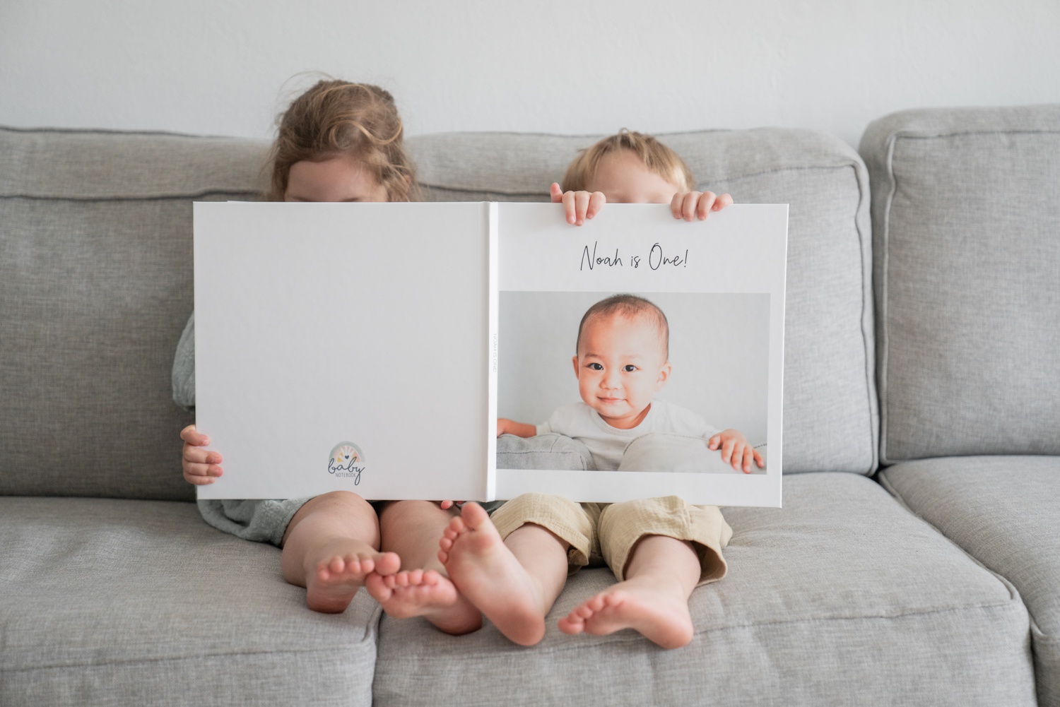 Two children sit side by side reading a toddler memory book.