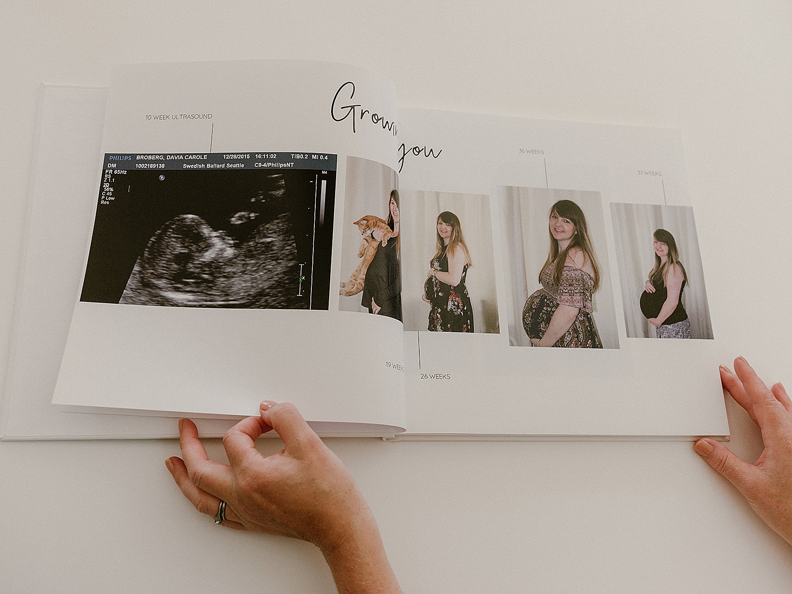 A woman opens a baby book to a page of maternity photos.