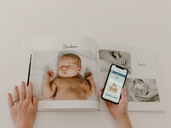 A woman holds a photo book maker app open in front of a custom baby book.