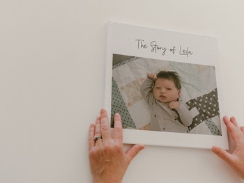 A woman's hands hold a baby memory book with a large photo of a newborn on the front.
