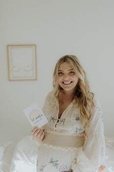 A woman smiles and holds a pregnancy card announcing how many weeks pregnant she is.