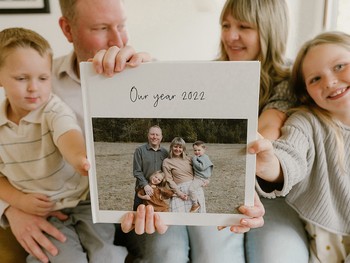 A family sits on a couch holding up their family yearbook.