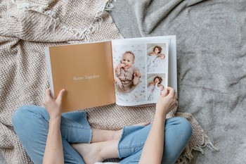 A woman sits on a bed and flips through a custom baby book.