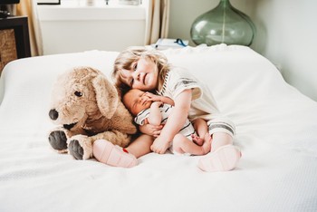 A child cuddles with her newborn sibling in DIY newborn photos.