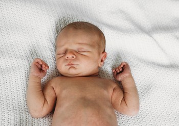 A newborn sleeps on his back in a newborn photo at home.