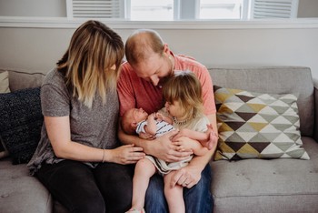 A mother and father hold their daughter and newborn for newborn photos at home.