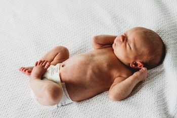 A newborn stretches on a white sheet.