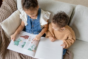 Two children sit in a chair looking at a custom baby book.