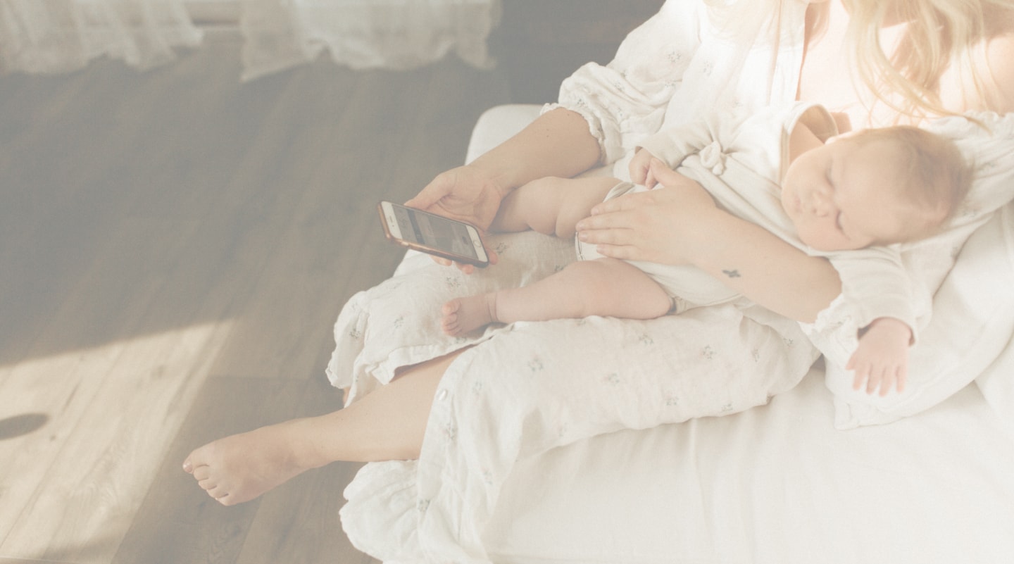 Mom sitting and holding sleeping baby on lap and filling out baby book app