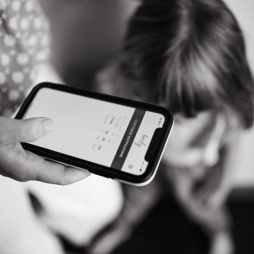 Hand holding a mobile phone showing customize notifications screen in the baby book app