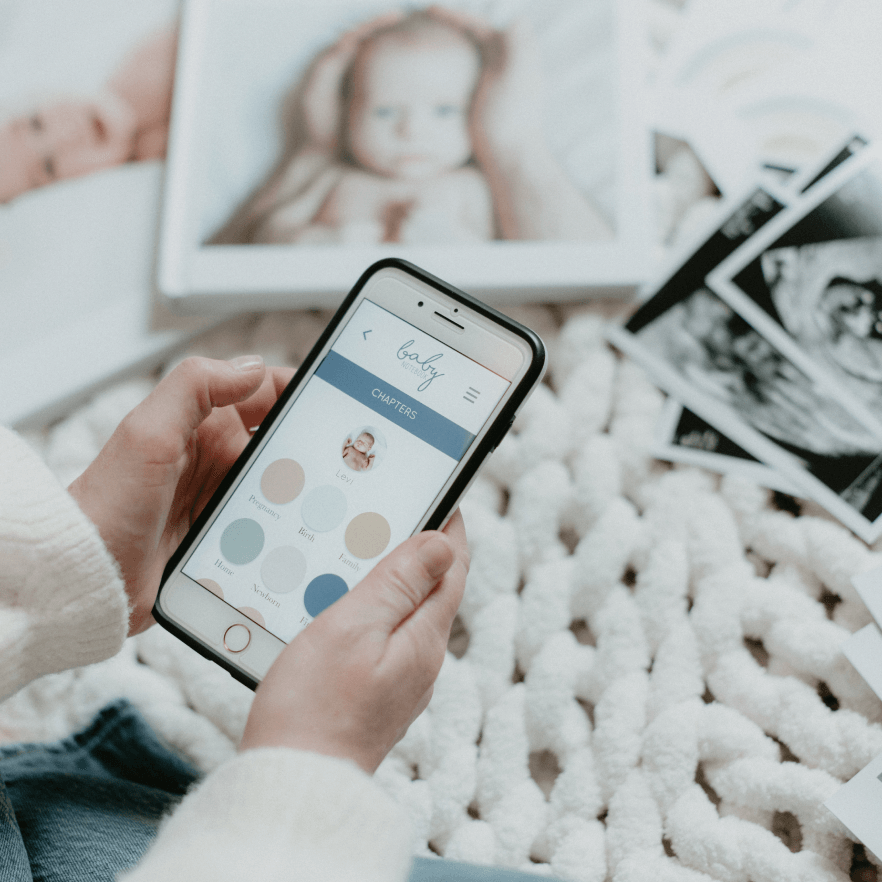 Hands holding a mobile phone showing a baby book app on the screen