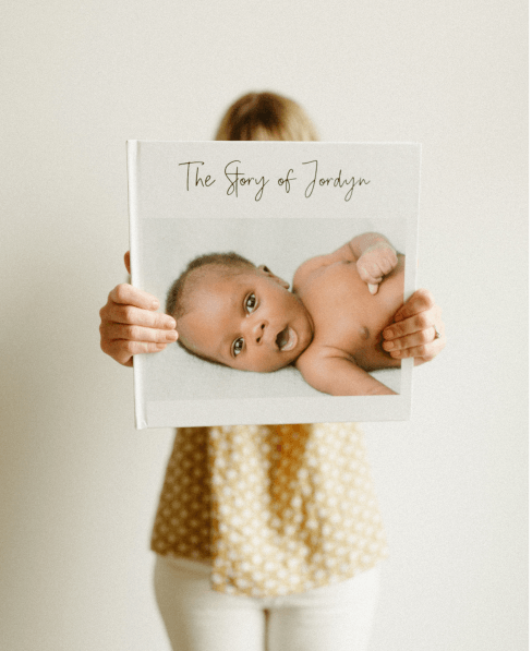 Mom holding baby's first year book with arms extended out in front of her showcasing cover